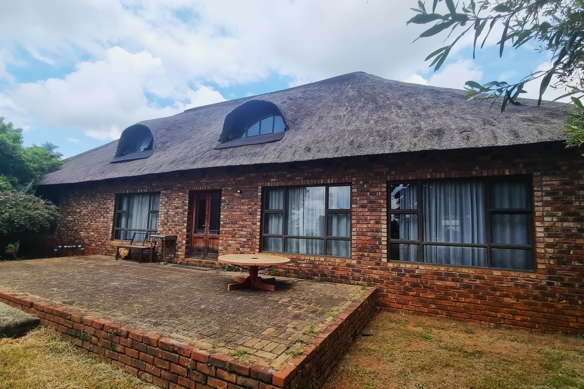 Rear view of a traditional face brick small holding home featuring a thatched roof, dormer windows, and a spacious paved patio area.