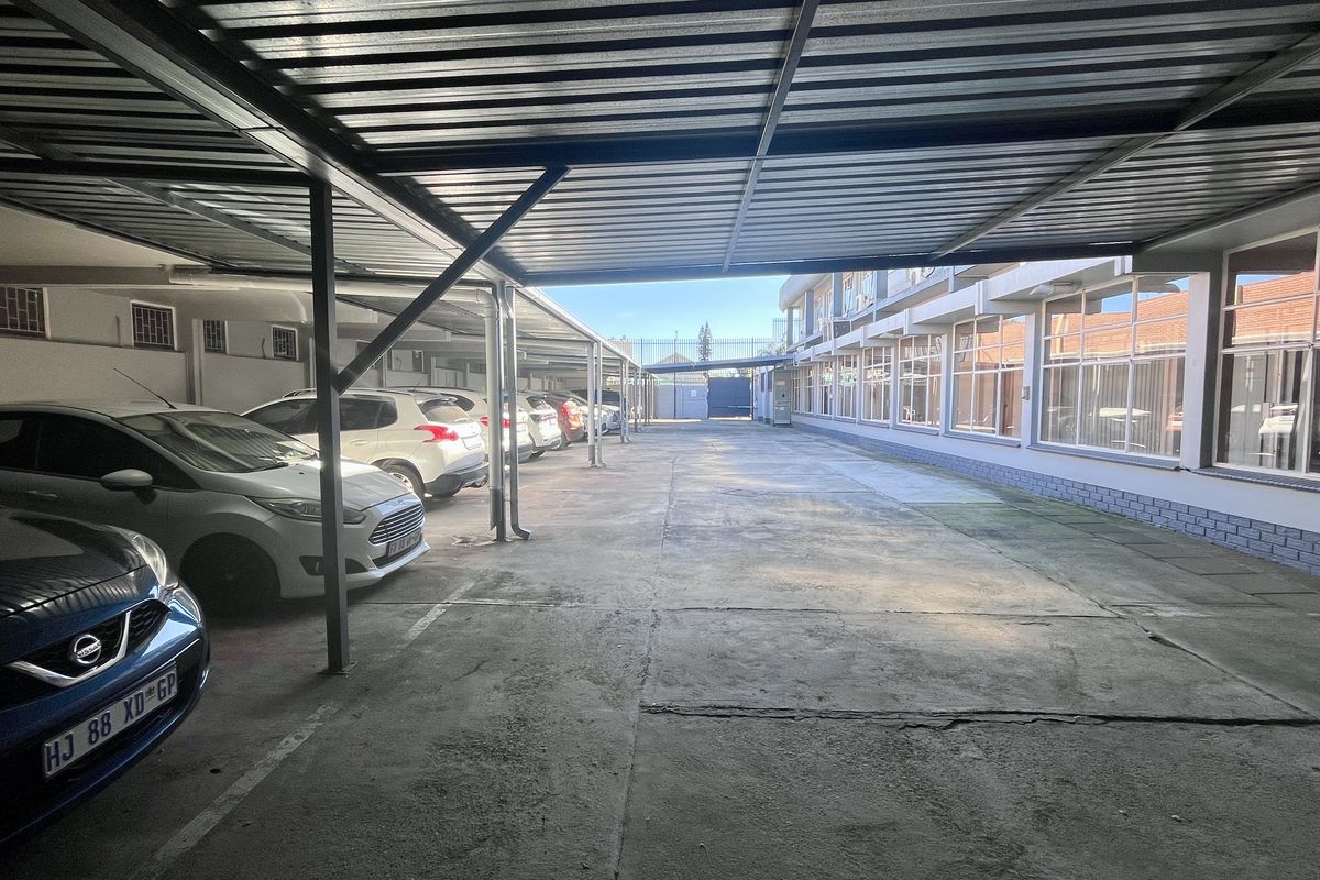 Covered parking area with metal roofing and concrete paving, adjacent to the office building with large windows.