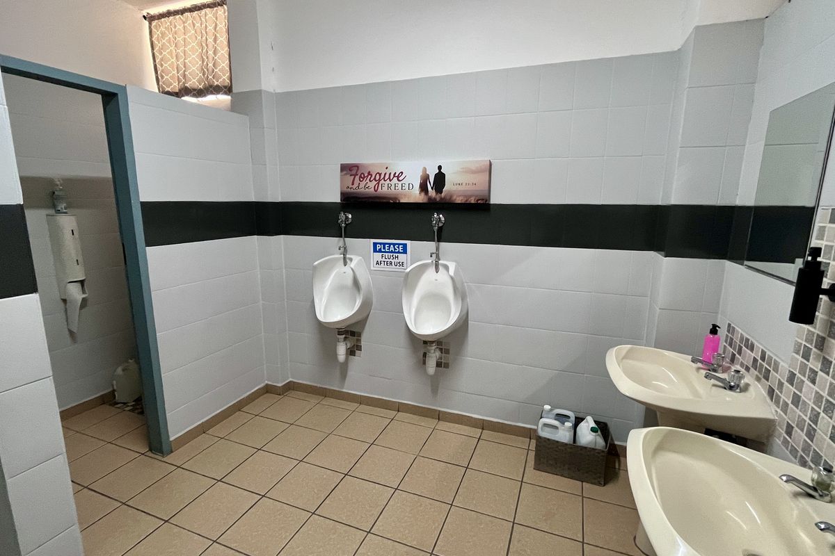 A functional office restroom featuring wall-mounted urinals, pedestal wash basins, and neutral ceramic wall and floor tiling.