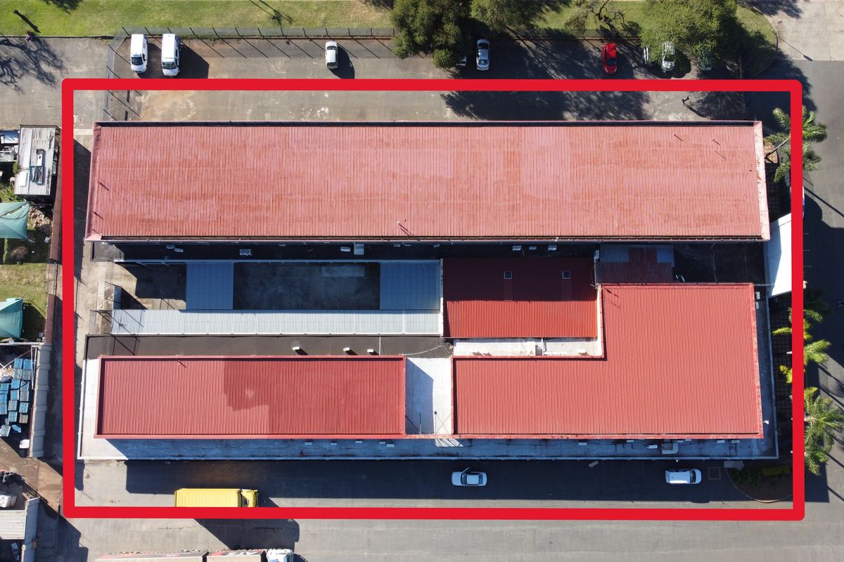 Aerial view of the office property featuring multiple corrugated metal roof sections and an adjacent asphalt parking area.