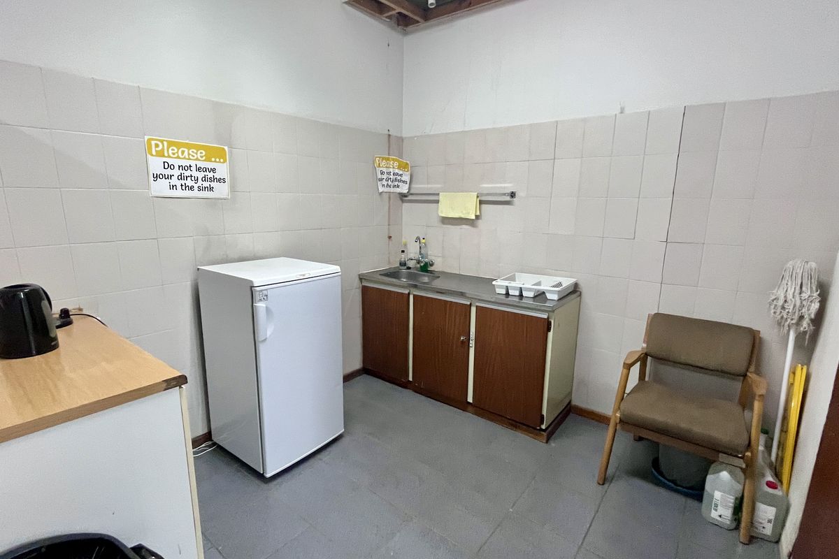 A functional office kitchenette featuring a stainless steel sink, tiled splashback, and built-in cabinetry, providing basic utility for staff.