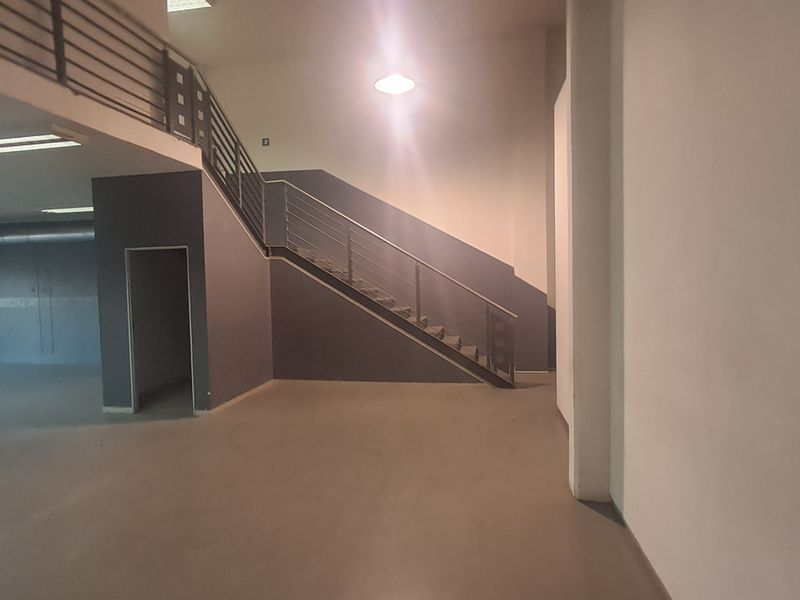 Spacious industrial open-plan area featuring a central staircase, mezzanine level, exposed ducting, and modern grey finishes, suitable for versatile commercial use.