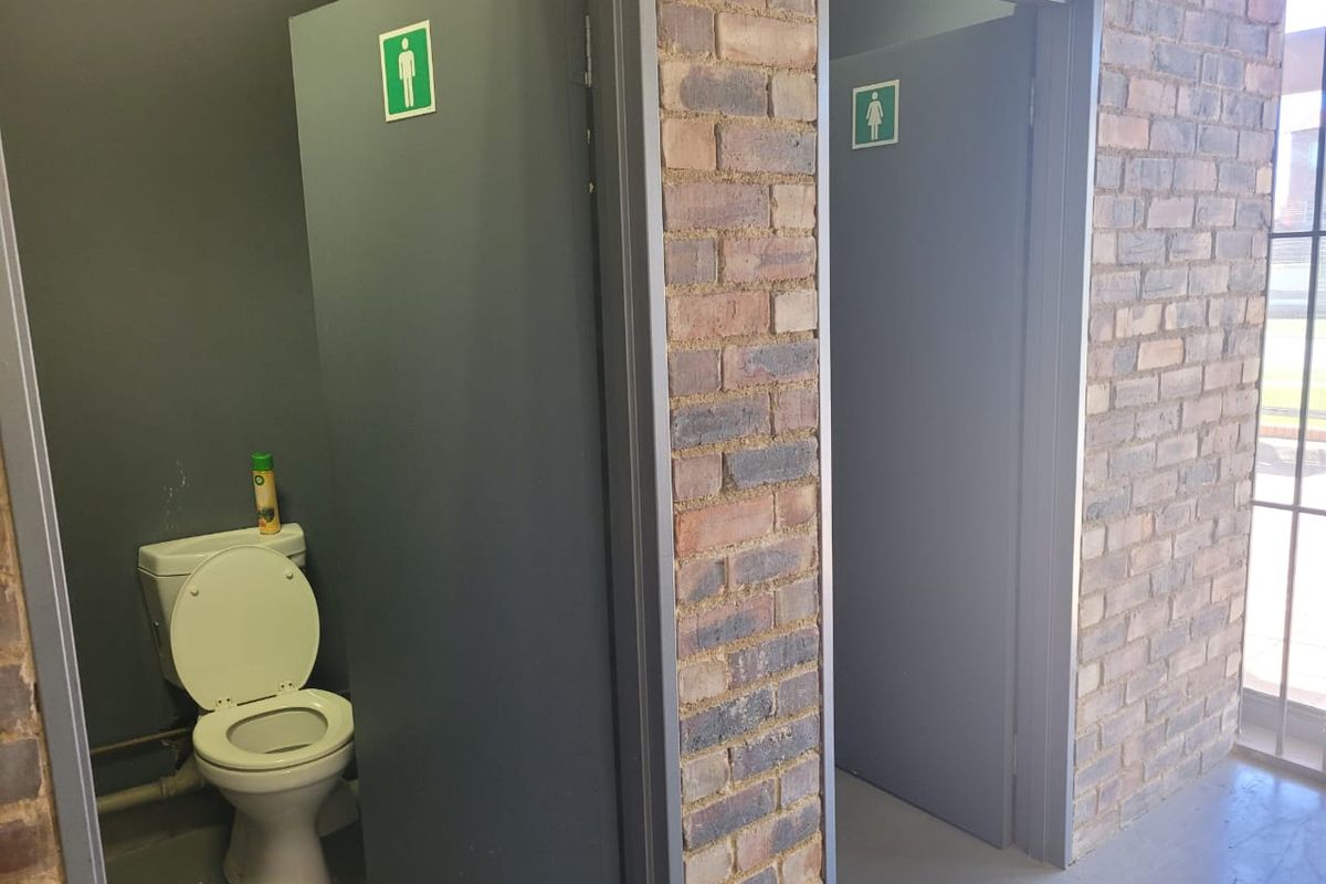 Industrial-style bathroom facility featuring exposed brick walls and separate gender-designated entrances with functional toilet fixtures.