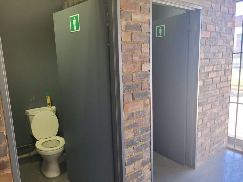 Industrial-style bathroom facility featuring exposed brick walls and separate gender-designated entrances with functional toilet fixtures.