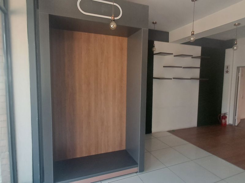 A modern commercial interior space featuring a mix of tiled and laminate flooring, built-in display shelving, and a recessed alcove with pendant lighting.