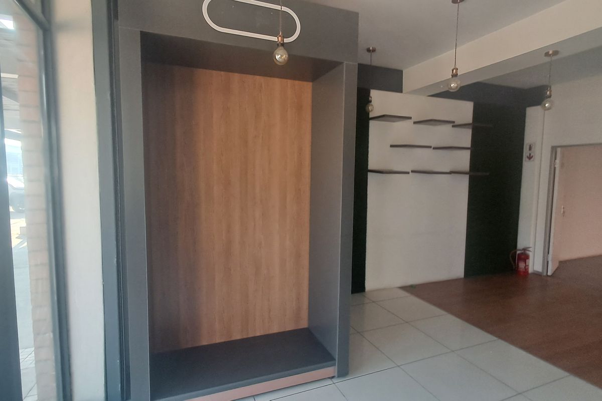 A modern commercial interior space featuring a mix of tiled and laminate flooring, built-in display shelving, and a recessed alcove with pendant lighting.