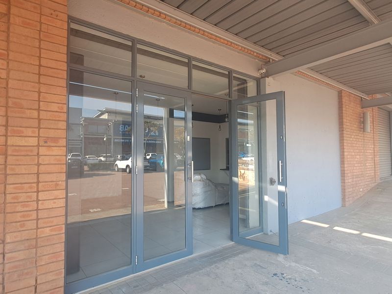 Industrial unit entrance featuring modern aluminium framed glass doors, exposed brickwork, and a covered walkway area.