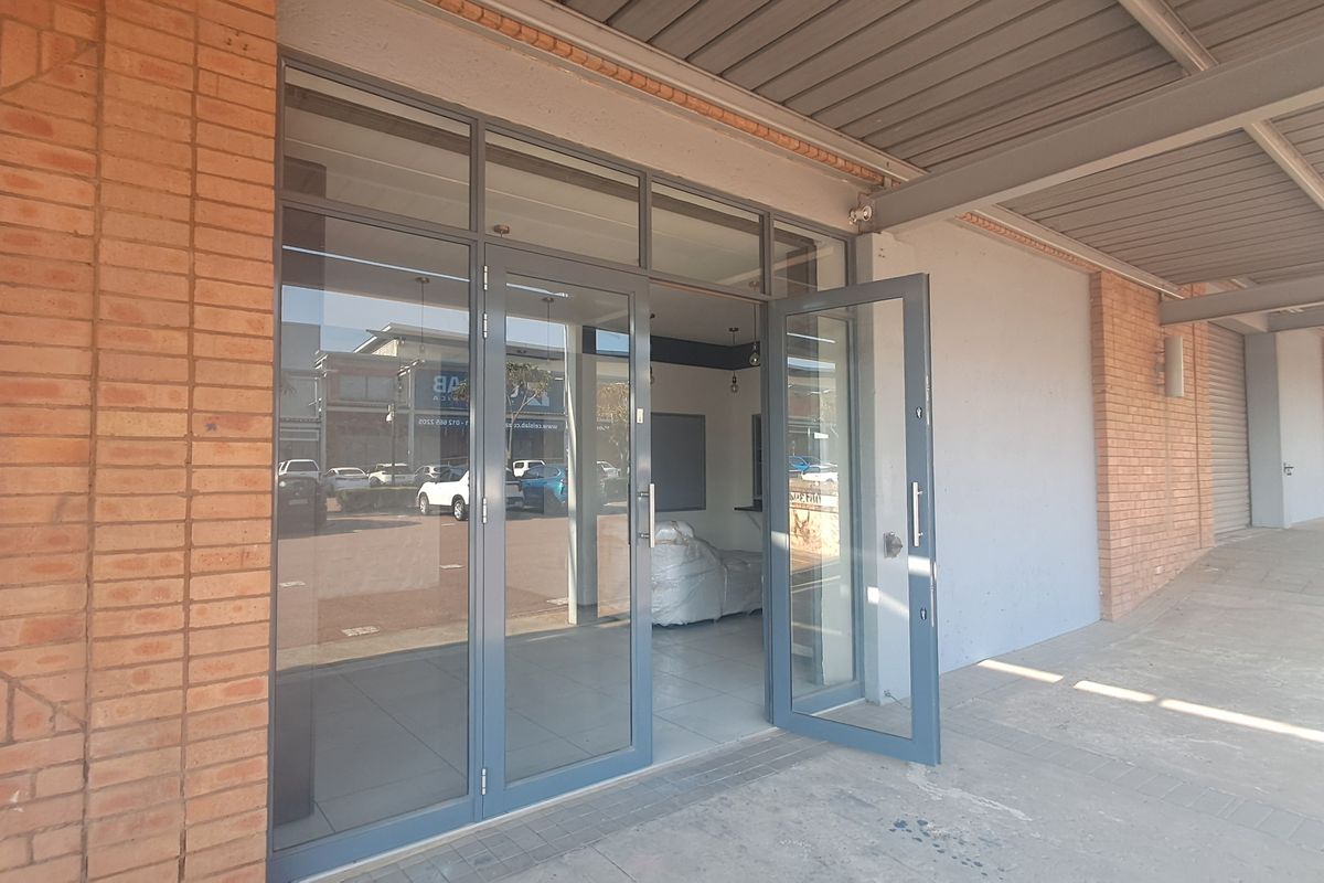 Industrial unit entrance featuring modern aluminium framed glass doors, exposed brickwork, and a covered walkway area.
