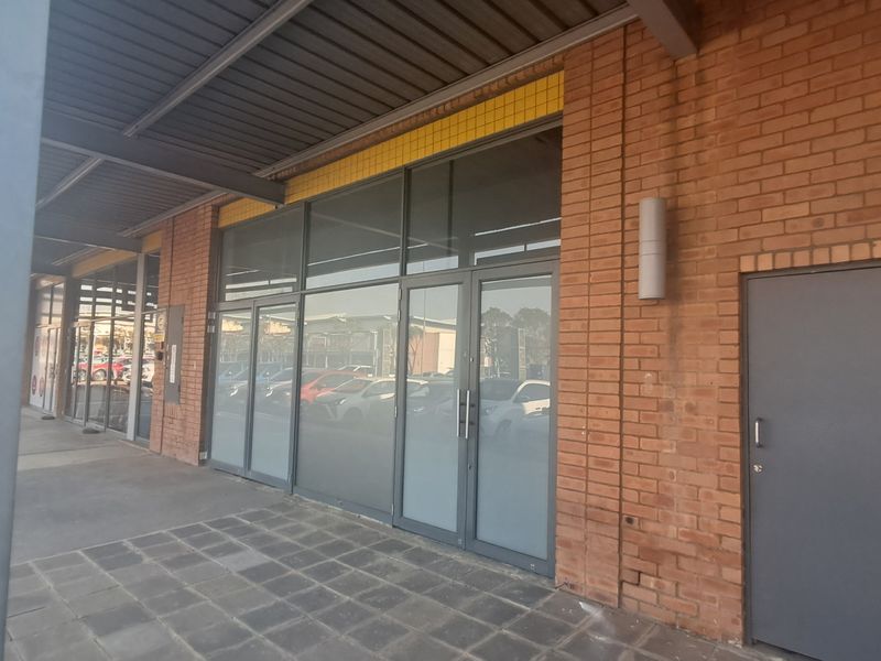 Front exterior view of an industrial unit featuring a brick facade, large glass storefront, and a covered paved walkway.