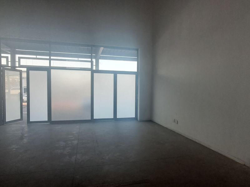 An empty industrial utility space featuring concrete flooring, high ceilings, and a large frosted glass storefront entrance.