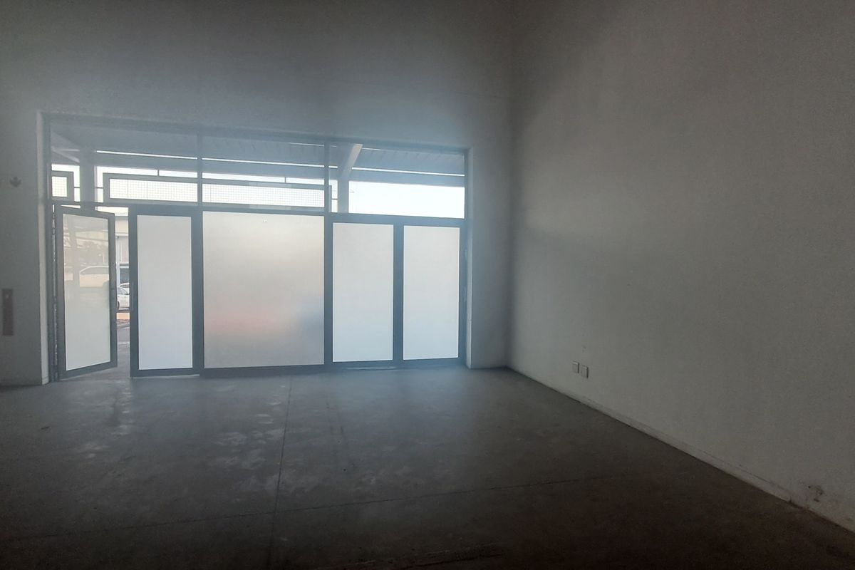 An empty industrial utility space featuring concrete flooring, high ceilings, and a large frosted glass storefront entrance.