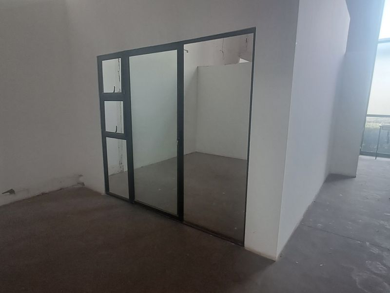 An empty industrial office space featuring a modern black aluminium framed glass partition and concrete flooring, suitable for a professional workspace.