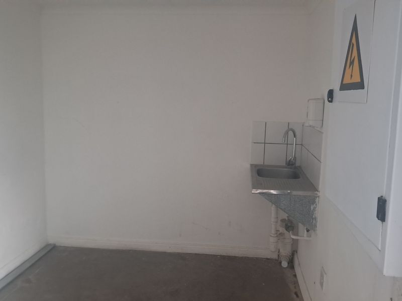 A functional utility space featuring a stainless steel sink, tiled splashback, and an electrical distribution board, suitable for industrial or workshop use.