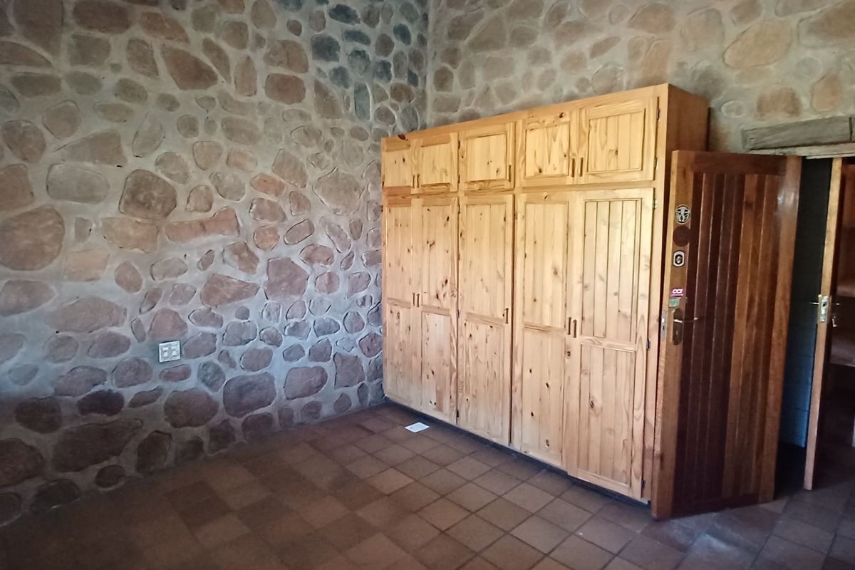 A rustic bedroom featuring exposed stone walls, tiled flooring, and extensive built-in wooden cabinetry, with an adjacent walk-in storage or closet area.