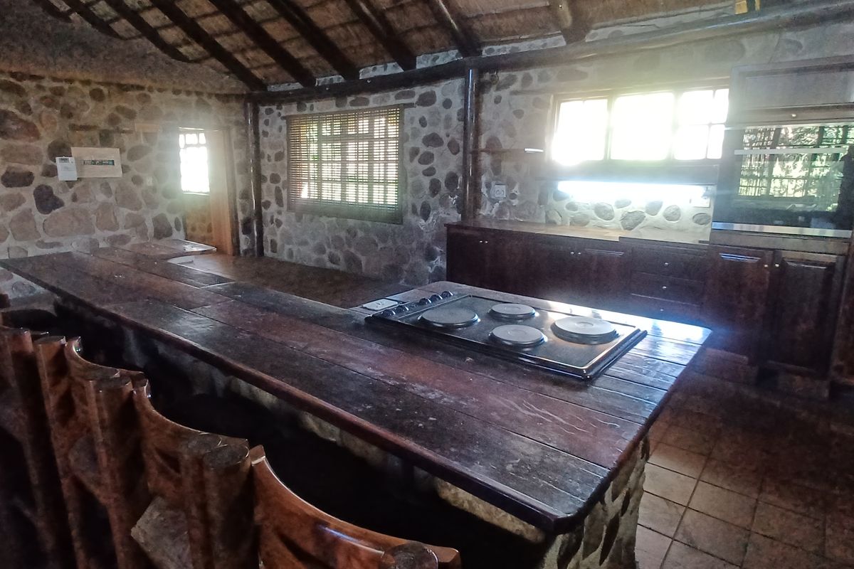 Rustic kitchen featuring stone walls, a thatched ceiling, built-in cabinetry, and a large stone breakfast bar with an integrated hob.