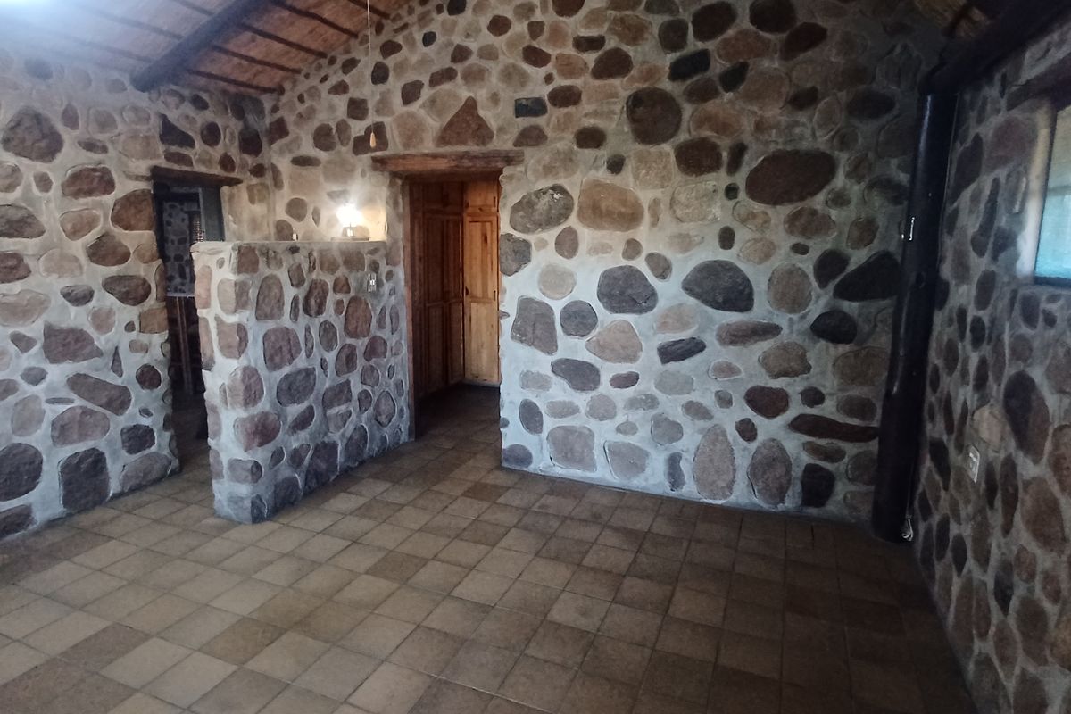 A rustic living area featuring distinctive exposed stone walls, tiled flooring, and an exposed timber beam ceiling, offering a unique character-filled space.