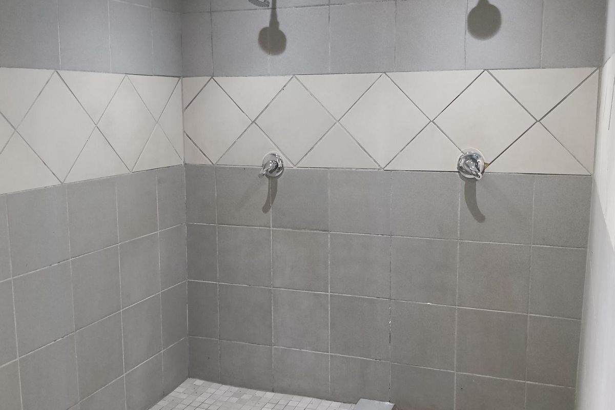 A functional industrial-style communal shower area featuring dual shower heads, tiled flooring, and wall-mounted fixtures.