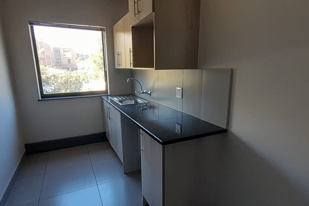 A compact kitchenette featuring dark granite countertops, light-toned cabinetry, a stainless steel sink, and tiled flooring.