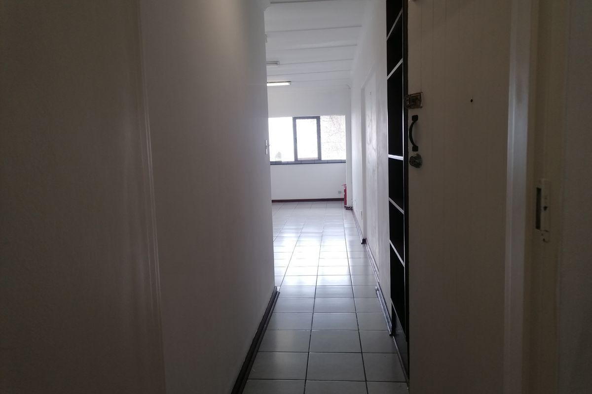 A functional office hallway featuring tiled flooring, built-in shelving, and direct access to an open-plan workspace area.