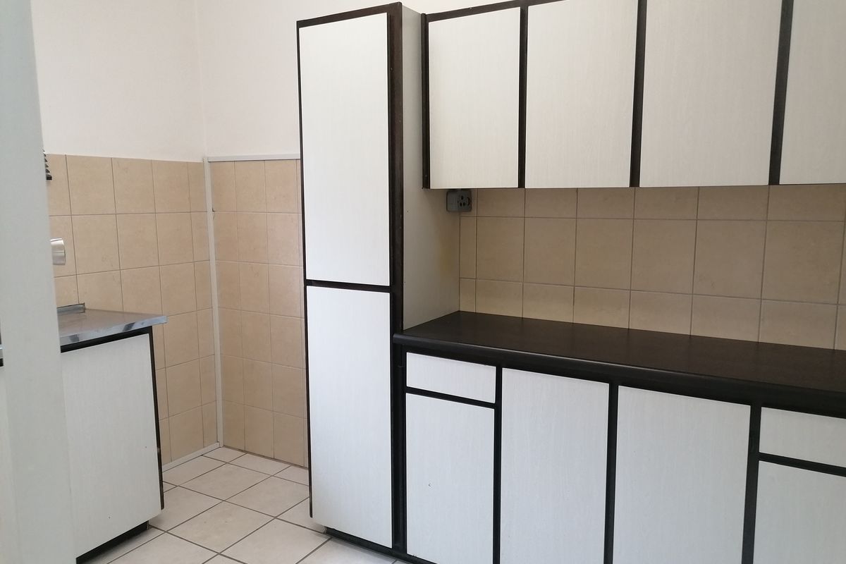 A functional kitchen area featuring built-in cabinetry, laminate countertops, tiled backsplash, and tiled flooring, offering a clean and practical workspace.
