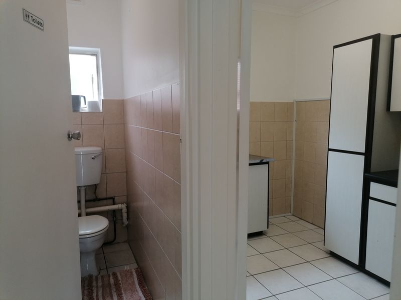 A functional office bathroom and adjacent utility area featuring tiled finishes and built-in cabinetry.