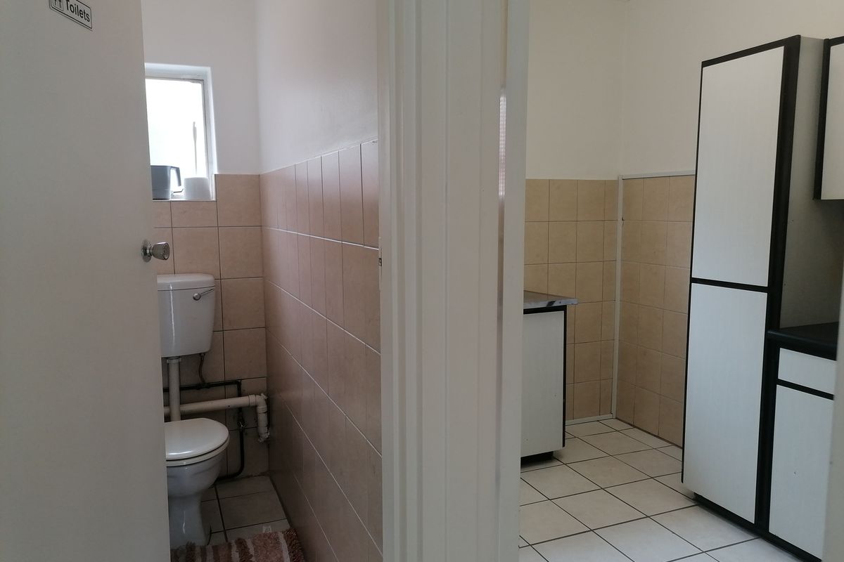 A functional office bathroom and adjacent utility area featuring tiled finishes and built-in cabinetry.