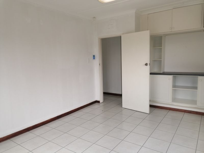 An empty office space featuring tiled flooring, built-in storage cabinetry, and neutral white walls, providing a clean and functional workspace environment.