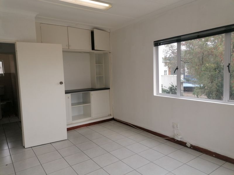 A functional office space featuring tiled flooring, built-in storage cabinetry, and large windows providing natural light.
