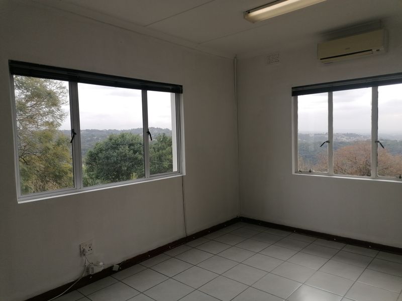 A vacant office space featuring tiled flooring, an air conditioning unit, and large windows offering scenic views.