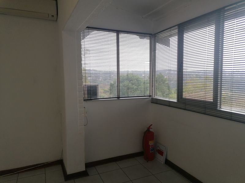 A bright, empty office space featuring tiled flooring, split-system air conditioning, and large windows with venetian blinds offering an elevated view.