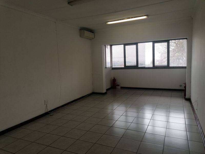 An empty, functional office space featuring tiled flooring, air conditioning, and large windows with venetian blinds, suitable for a professional workspace.