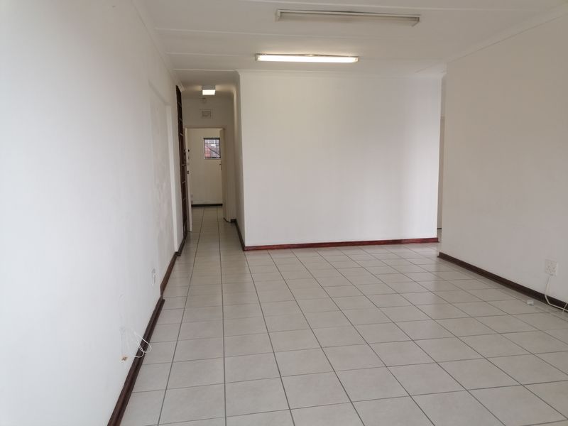 An empty, open-plan office space featuring neutral ceramic floor tiles, fluorescent lighting, and clean white walls, suitable for a professional workspace.