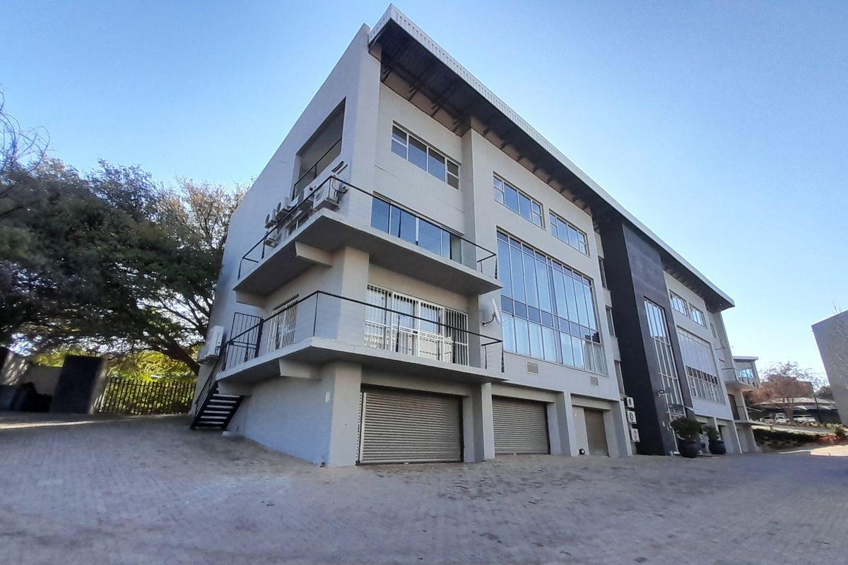 A multi-story office building featuring a modern facade, large glass windows, multiple balconies, and ground-level roller shutter garage doors.