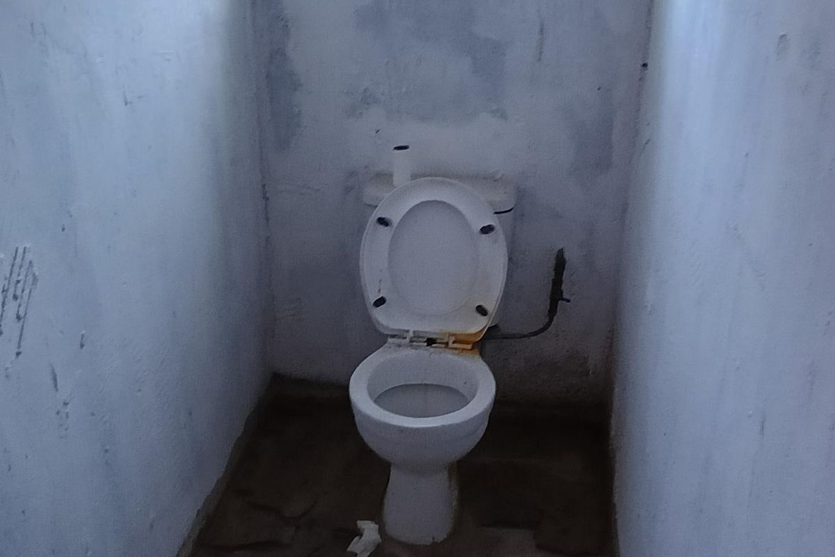 A small, dilapidated bathroom featuring a toilet, requiring significant renovation and repair to the flooring and wall finishes.