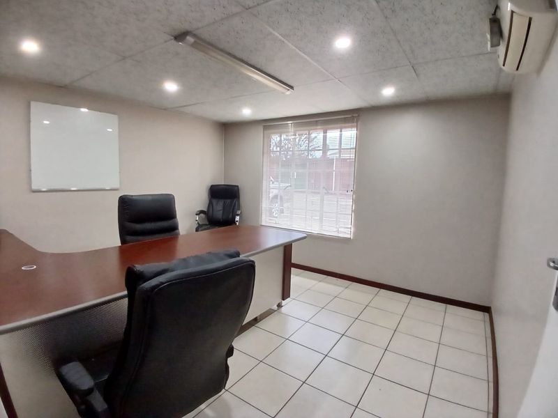 A functional commercial office space featuring ceramic tiled flooring, a suspended ceiling with integrated lighting, and a wall-mounted air conditioning unit.