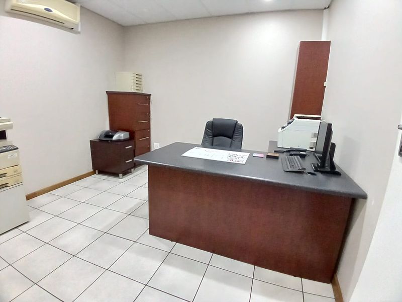 A functional office space featuring tiled flooring, a suspended ceiling, and a wall-mounted split-system air conditioning unit.