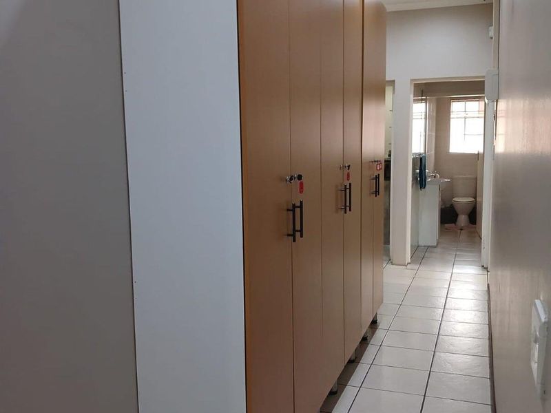 A functional hallway featuring built-in storage lockers, tiled flooring, and recessed lighting, leading towards a bathroom area.