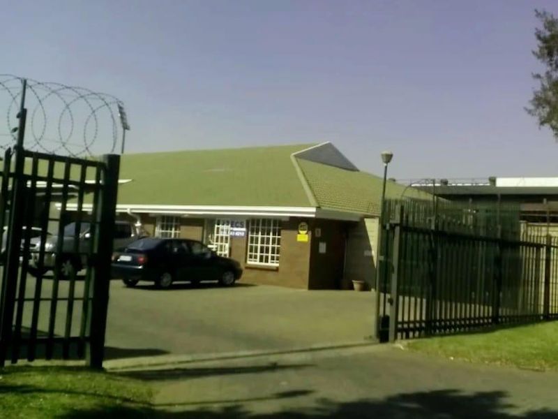 Front exterior view of a commercial property featuring a brick facade, tiled roof, and secure perimeter fencing with a gated entrance.