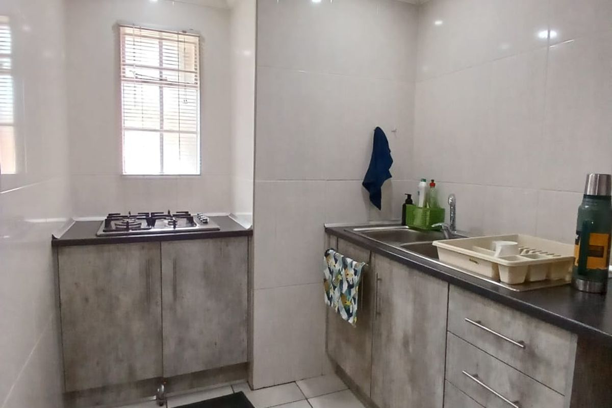 Compact kitchen featuring modern grey cabinetry, a gas hob, stainless steel sink, and clean tiled finishes throughout.