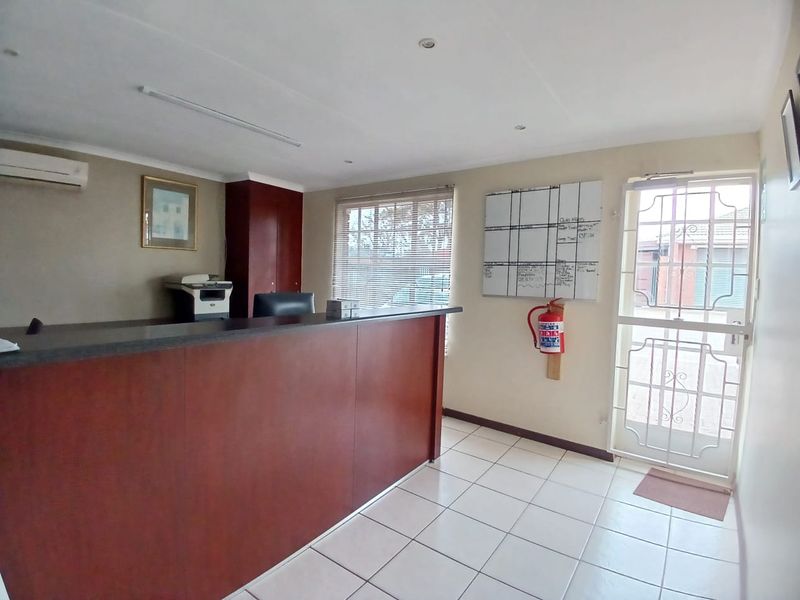 A functional commercial office space featuring a built-in reception desk, tiled flooring, air conditioning, and a secure entrance door.