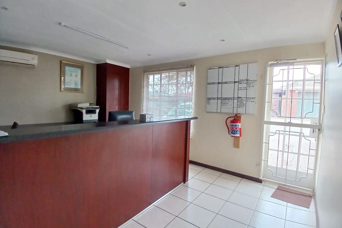 A functional commercial office space featuring a built-in reception desk, tiled flooring, air conditioning, and a secure entrance door.