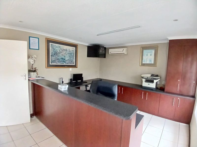 A functional commercial office space featuring a built-in reception desk, ample storage cabinetry, tiled flooring, and a wall-mounted air conditioning unit.