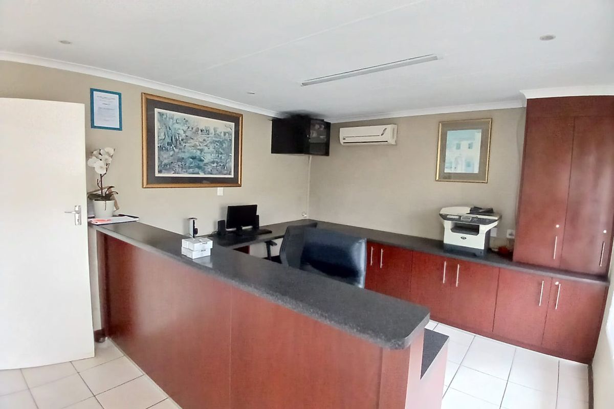 A functional commercial office space featuring a built-in reception desk, ample storage cabinetry, tiled flooring, and a wall-mounted air conditioning unit.