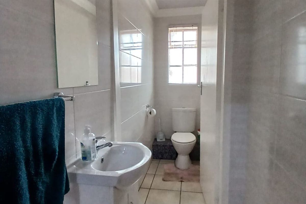 A functional bathroom featuring a pedestal washbasin, tiled walls and flooring, and a separate toilet area with natural light.