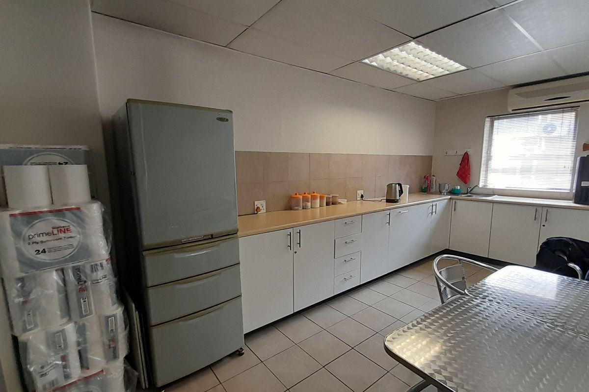 Functional office kitchenette featuring white cabinetry, tiled backsplash, and integrated sink, providing a practical break area for staff.