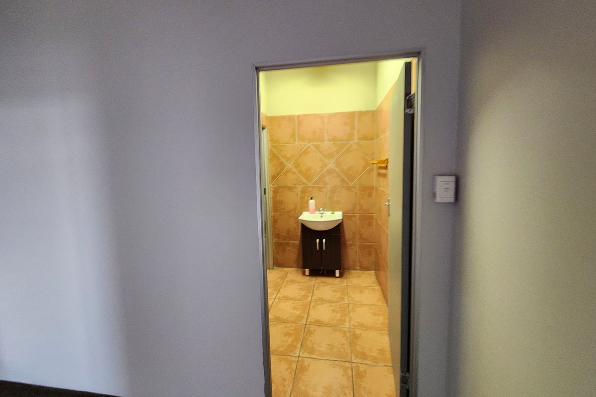 A functional industrial restroom featuring a wall-mounted basin with a vanity cabinet and tiled flooring.