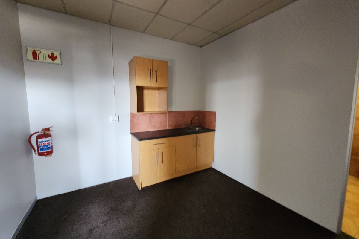 A functional kitchenette area featuring built-in wooden cabinetry, a small sink, and tiled splashback, suitable for office or industrial utility use.
