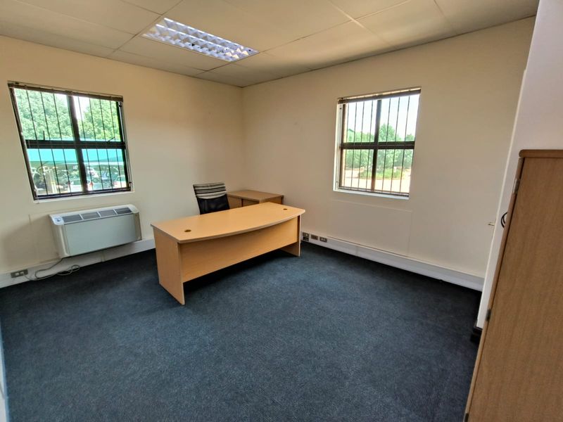 A functional office space featuring carpeted flooring, recessed ceiling lighting, security bars on windows, and a wall-mounted air conditioning unit.