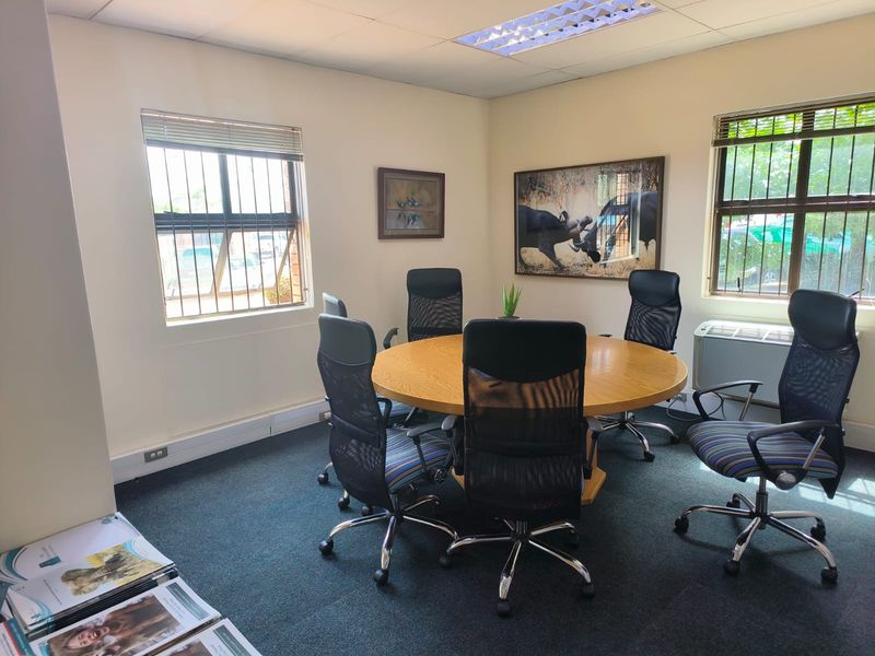 A functional office meeting room featuring carpeted flooring, recessed lighting, security bars on windows, and a built-in air conditioning unit.