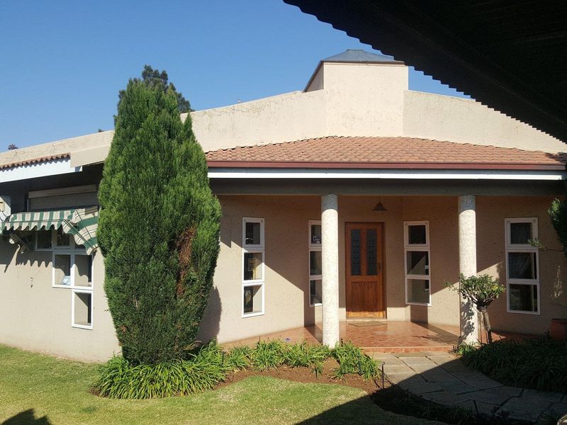 Front elevation of a commercial property featuring a covered porch, stone columns, and a tiled roof with a well-maintained garden area.